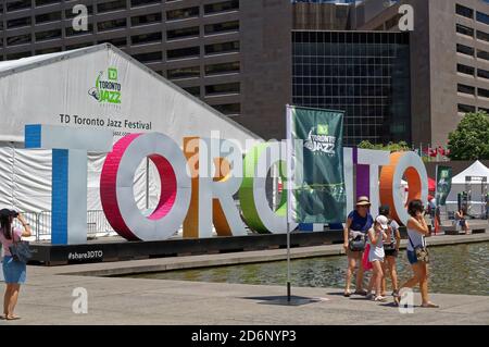 TORONTO, CANADA - 06 27 2016: People walking in front of TORONTO sign and the concert hall pavilion of Toronto Jazz Festival in the Nathan Phillips Stock Photo