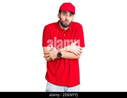 Young handsome man with beard wearing delivery uniform shaking and freezing for winter cold with sad and shock expression on face Stock Photo