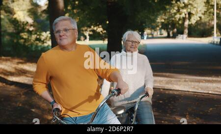 Senior couple riding double bicycle in autumn. Grandmother and grandfather cycling together . Elderly people healthy and active lifestyle. High quality photo Stock Photo