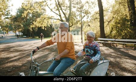 Senior couple riding double bicycle in autumn. Grandmother and grandfather cycling together . Elderly people healthy and active lifestyle. High quality photo Stock Photo