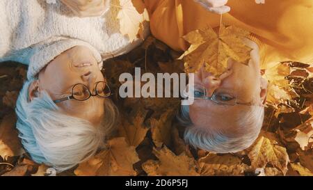 Elderly couple lying on the forest ground and playing with yellow autumn leaves. Love and romance in old age. High quality photo Stock Photo
