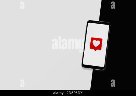 Top view of cell phone with heart emoticon. Minimalist design. White screen and black and white background, copy space. Social network concept. Stock Photo