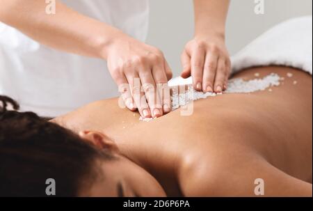 Therapist applying sea salt on black female patient spine Stock Photo