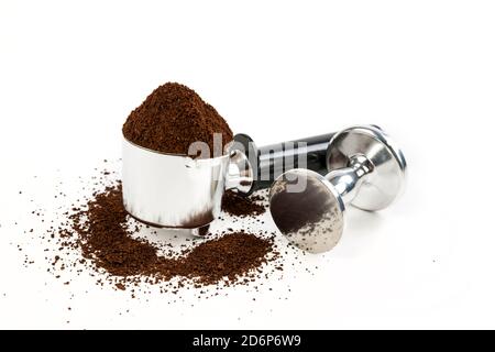 Black and silver coffee filter piled high with grounds sitting next to a tamper over a white background Stock Photo