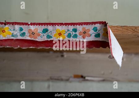 Torn, peeling wallpaper border is ripped against the wall. Useful for abstract backgrounds. Floral, colors of red, green and yellow Stock Photo
