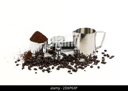 Black and silver coffee filter piled high with grounds sitting next to a tamper and milk steamer cup, beans surround the base Stock Photo