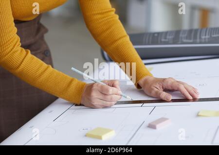 Side view close up of unrecognizable female architect drawing blueprints while leaning on desk at workplace, copy space Stock Photo