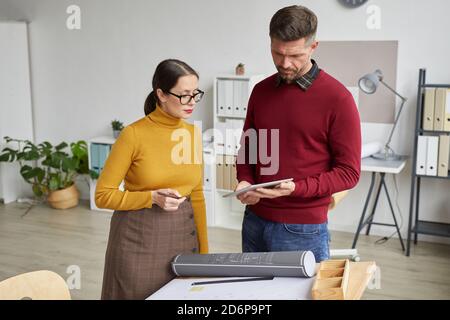 Waist up portrait of two architects using digital tablet while working on blueprints together in office, copy space Stock Photo