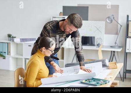 Side view portrait of two architects collaborating on blueprints while working in office together, copy space Stock Photo