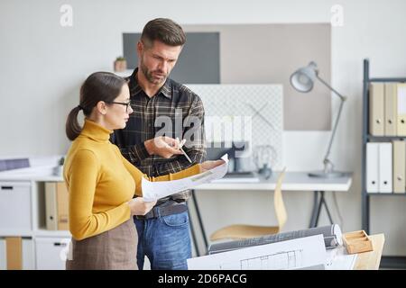 Side view portrait of two architects discussing blueprints while working in office together, copy space Stock Photo