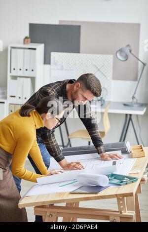Vertical side view portrait of two architects cdrawing blueprints while working in office together Stock Photo