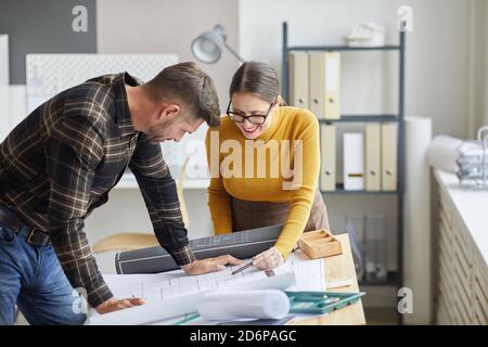 Portrait of two architects collaborating on blueprints while standing by drawing desk and working in office together, copy space Stock Photo
