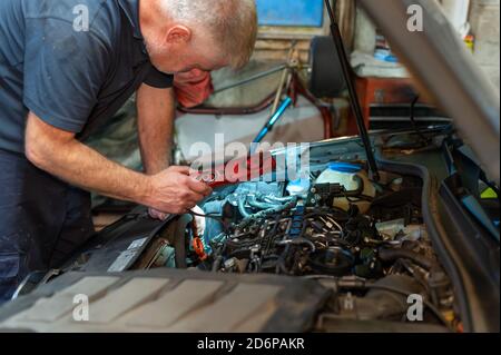 Senior Mechanic working on engine bay repairing a oil leak in home garage Stock Photo