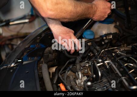 Senior Mechanic working on engine bay repairing a oil leak in home garage Stock Photo