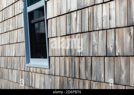 An external cedar wood wall with a closed blue trim glass window. The walls are textured with brown and tan colored shades on the wood. Stock Photo