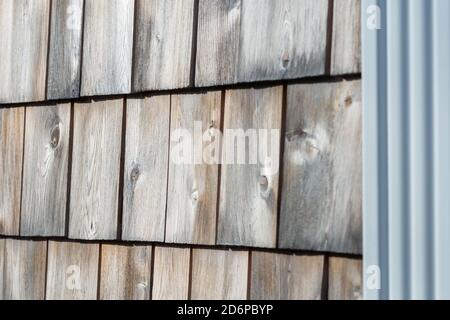 Natural white cedar shakes siding worn and textured on an exterior wall of a building. The thick smooth wood has faded in the sun. Stock Photo