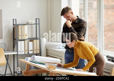 Side view portrait of two architects looking at floor plan while working on blueprints at workplace, copy space Stock Photo