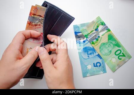 A person opening a wallet and spending canadian dollars on a white background. Concept: Spending Money Stock Photo