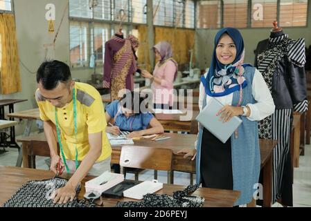 Muslim woman tailor in veiled standing with holding tablet pc beside the male tailor at the clothing production room Stock Photo