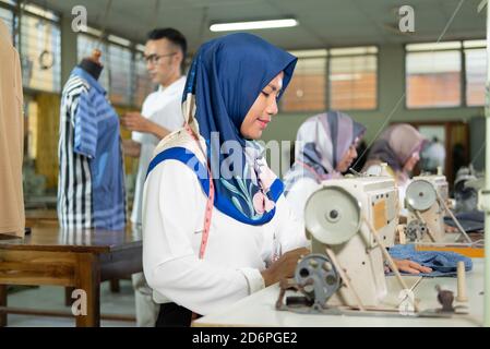 close up female tailor in hijab using a sewing machine while working at garment room Stock Photo