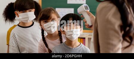 Banner group of diverse students in school building checked and scanned for temperature check. Elementary pupils are wearing face mask, line up before entering into classroom. Covid-19 school reopen Stock Photo