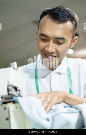Asian male tailor sew meticulously using a sewing machine in a garment factory Stock Photo
