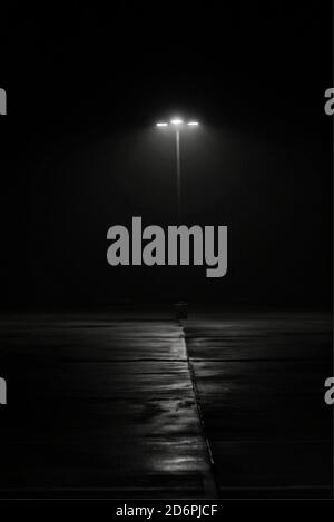 Street lamp on foggy night. Film noir feel with a sense of mystery and intrigue and shadowy textures on the ground. Minimalist image with copy space. Stock Photo