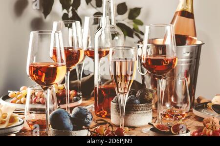 Rose wine glasses and bottles on table served for festive dinner party with different kinds of appetizers and fruits Stock Photo