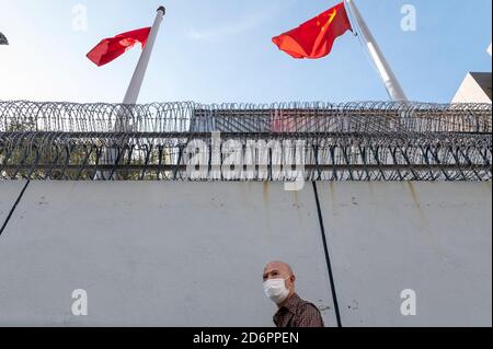 Hong Kong, China. 15th Oct, 2020. A pedestrian wearing a face mask walks past a police station as Hong Kong and China flags wave with the wind. Credit: SOPA Images Limited/Alamy Live News Stock Photo