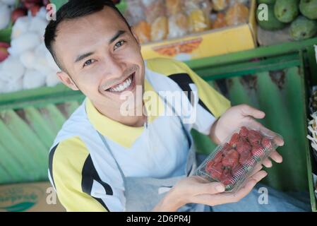 Smiling male salesman carrying a packet of strawberries in two hands at a fruit shop Stock Photo