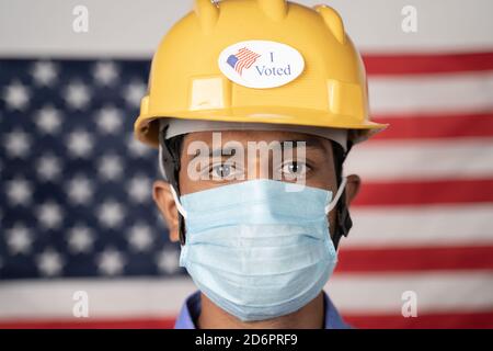 Head shot, I voted sticker on worker hardhat with US flag as background - Concept of USA elections and voting. Stock Photo