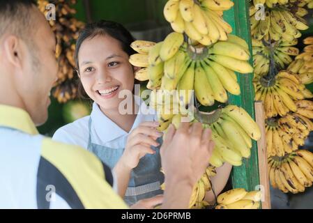 lady shop assistant offers bananas to customers at a fruit stand in a market Stock Photo