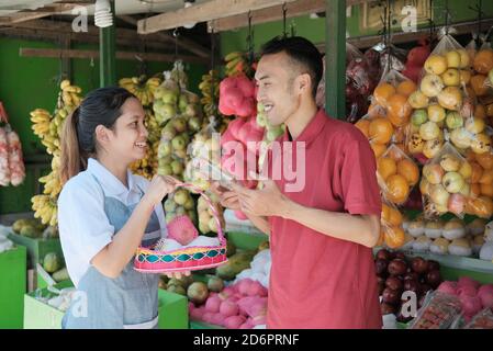 Asian female shopkeeper in apron give service for male customers want to buy fruit parcels in the fruit market Stock Photo