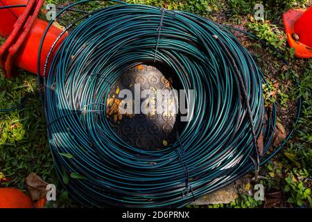 Top down view of a big coil of fiber optics dark colour cables coiled up and placed on the drainage cover with light and shadows around it. Singapore Stock Photo