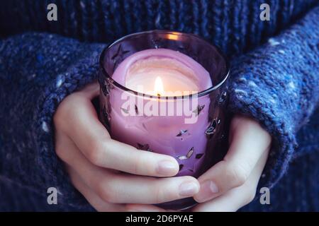 Girl in soft warm dark blue knitted sweater holds in hands burning candle. Christmas candle. Waiting for the holiday Stock Photo