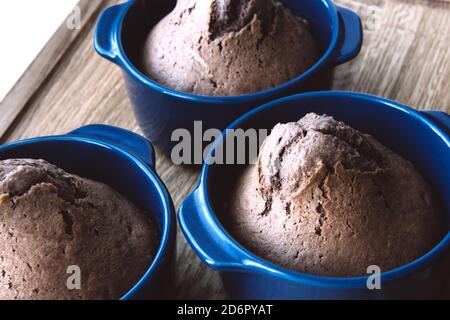 Delicious baked chocolate muffins in blue ceramic tins on wooden background. Side view Stock Photo