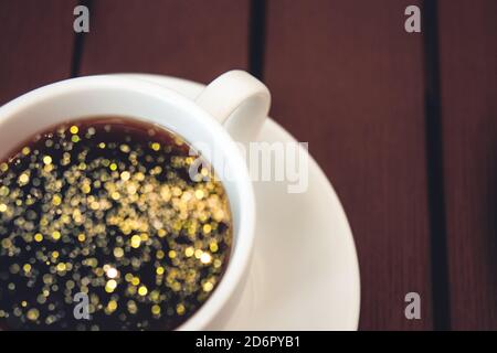 Magic golden blur in the cup. Wonderful black coffee in a white ceramic cup on a wooden table. Breakfast in a cafe Stock Photo