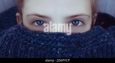Beautiful girl with blue eyes wrapped herself in a warm blue knitted sweater Stock Photo