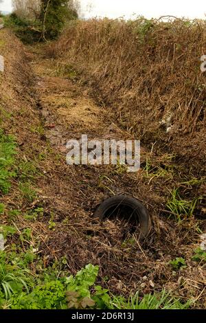 October 20 - Old car tyre dumped in a Freshly excavated and cleaned out roadside drainage ditch in Autumn. Stock Photo