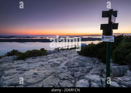 Path pointers on the Kamenjak hill. Panorama of Vrana lake at sunset, a view to the coast and Kornati islands in a distance Stock Photo
