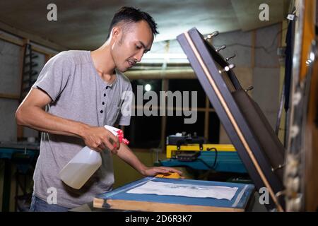 asian man worker use oil spray when preparing screen printing film in workshop Stock Photo