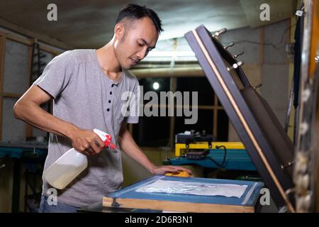 Male worker using sprayer to to paste the paper when going to make a film on the silkscreen Stock Photo
