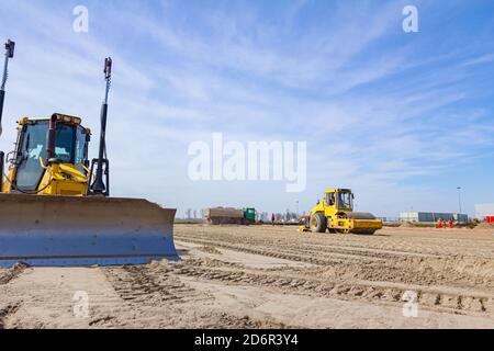 Vibration plate compactor is mounted to the steamroller, compacting sand at road construction site. Stock Photo