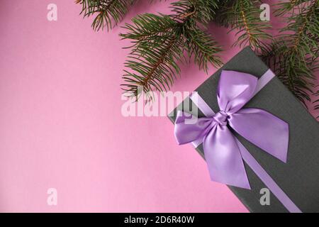 new year's Christmas holiday background a branch of spruce pine trees and a festive box black with purple purple ribbon and bow on a pink light backgr Stock Photo