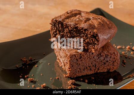 Two slices of chocolate brownies on a black plate on wooden table. Stock Photo