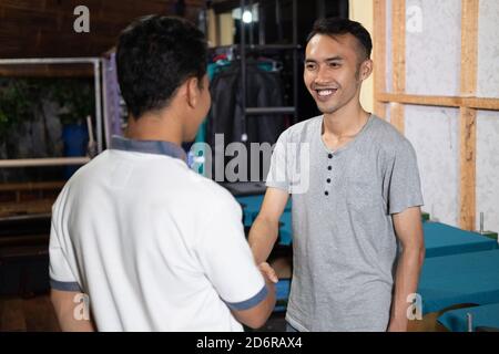 smiling Asian male owner shaking hands when meeting customers at the screen printing office Stock Photo