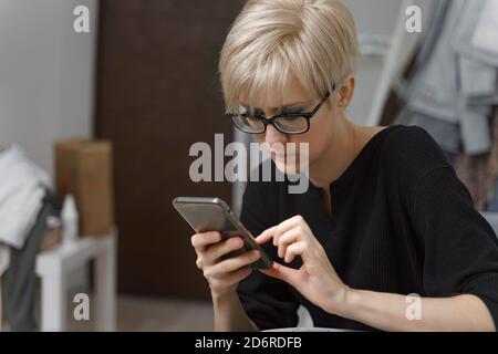 portrait of a beautiful young blonde woman wearing glasses using her mobile phone at home Stock Photo