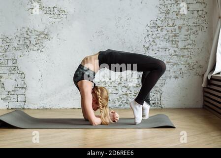 Cute blonde is engaged in fitness on the background of a white brick wall at home during quarantine. Stay home and exercise your body. Stock Photo