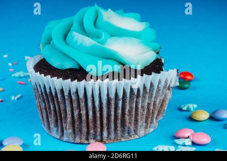 Chocolate Cupcake with whipped cream in a blue background, decorated with sugar snowflakes, sprinkles, colorful candies, holiday concept, greeting car Stock Photo