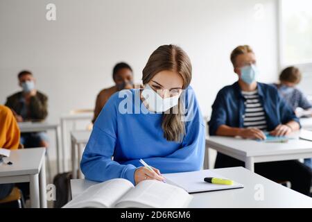 Young students with face masks at desks at college or university, coronavirus concept. Stock Photo